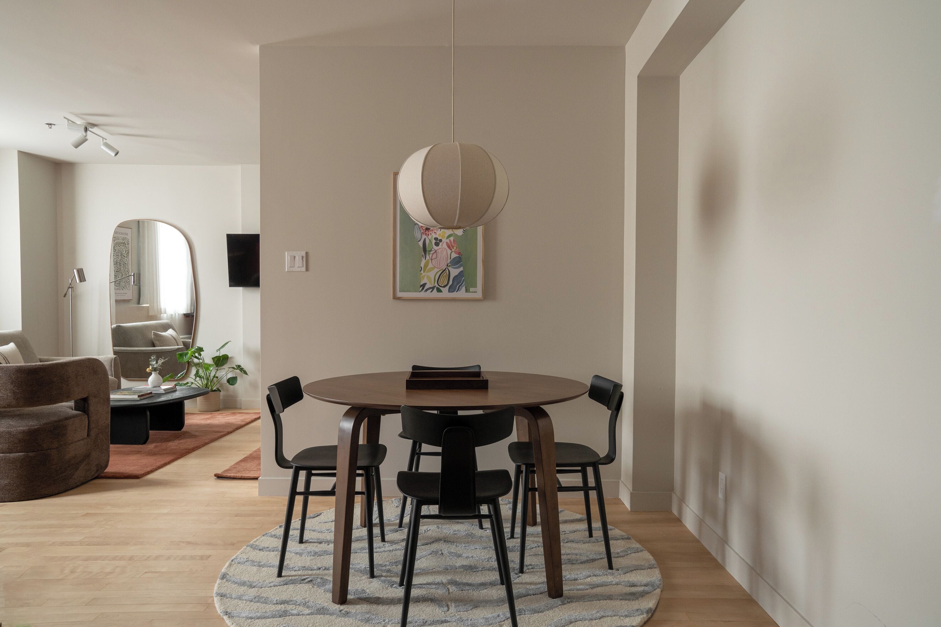 En matplats med ett runt bord, fyra stolar, en hängande lampa, ett inramat konstverk och en krukväxt.
