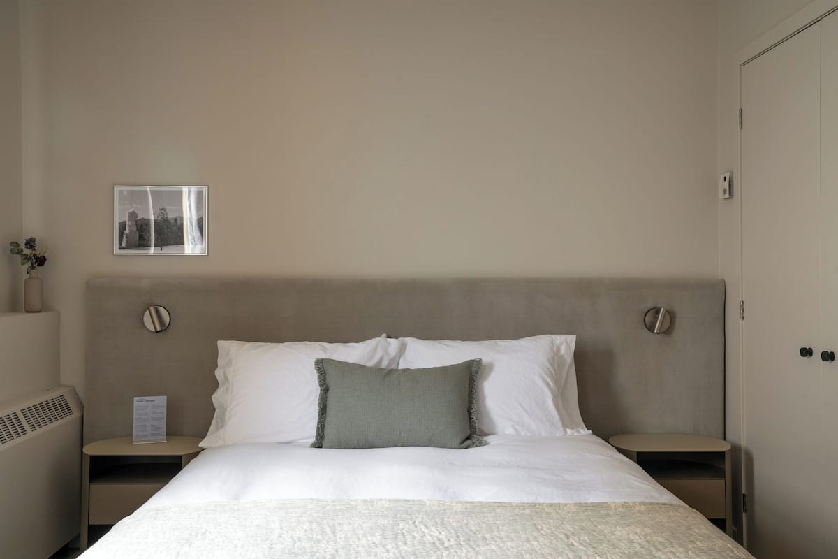 A hotel room with a bed, a nightstand, a wall-mounted picture, and a door.