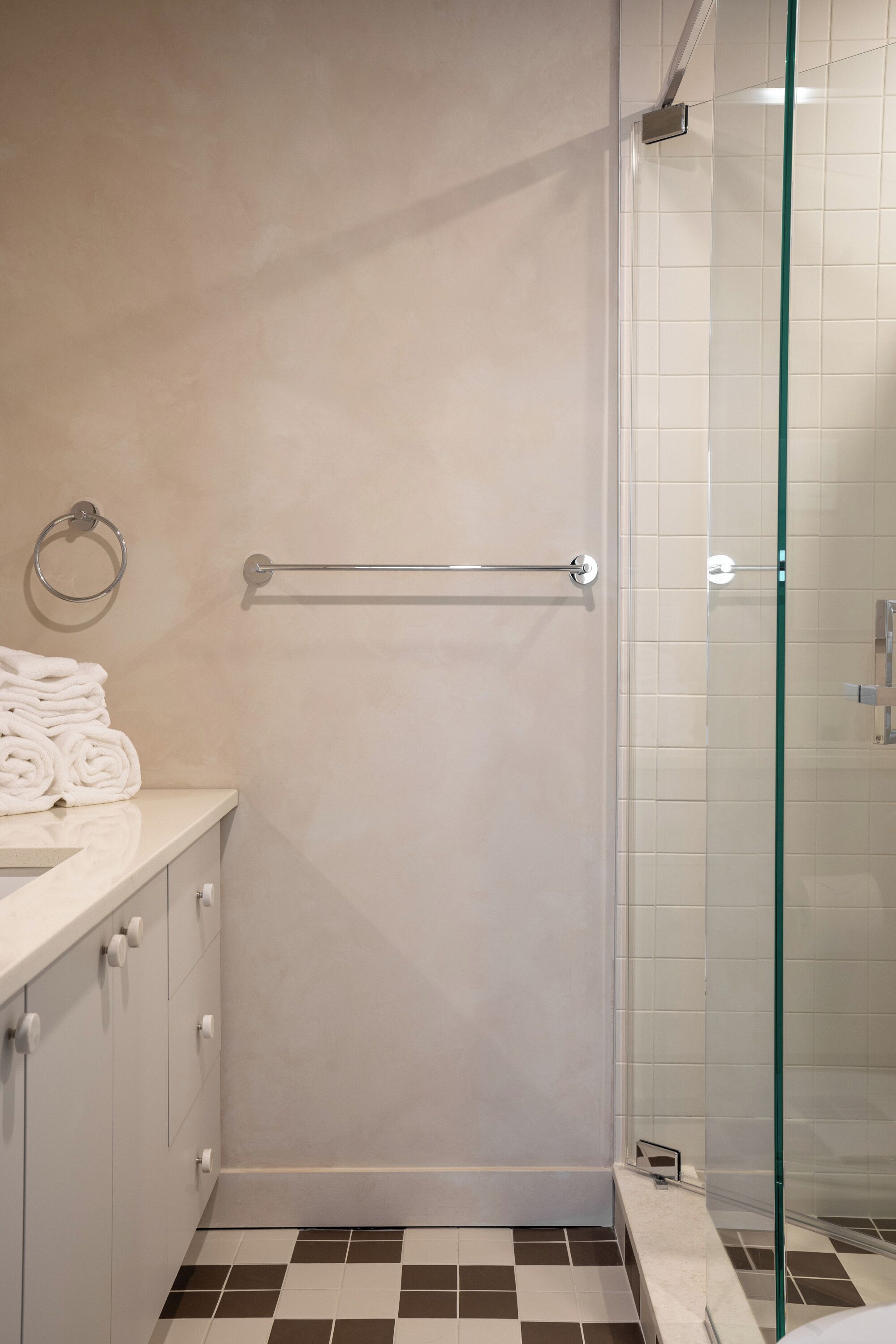 Un baño con cabina de ducha de vidrio, un perchero y un lavabo con encimera blanca.