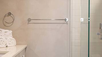 Un baño con cabina de ducha de vidrio, un perchero y un lavabo con encimera blanca.