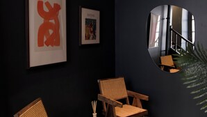A room with two wooden chairs, a small table, and a framed artwork on the wall.