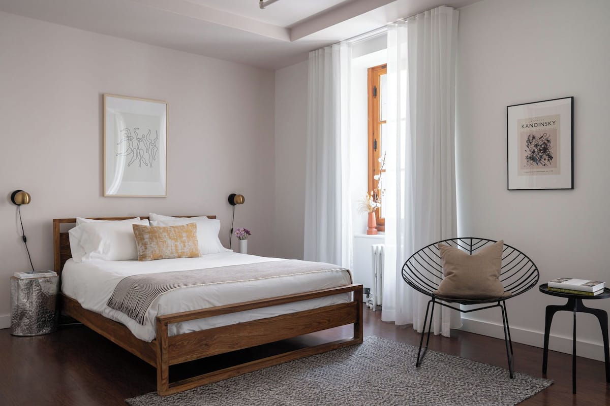A bedroom with a wooden bed, white bedding, a round black chair, and two framed artworks.