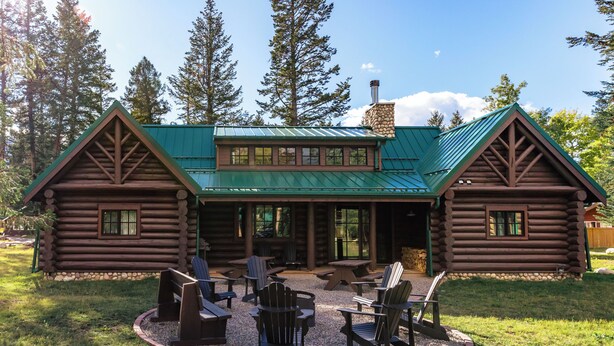Una cabaña de madera con techo verde, varias ventanas y un patio con mobiliario exterior.