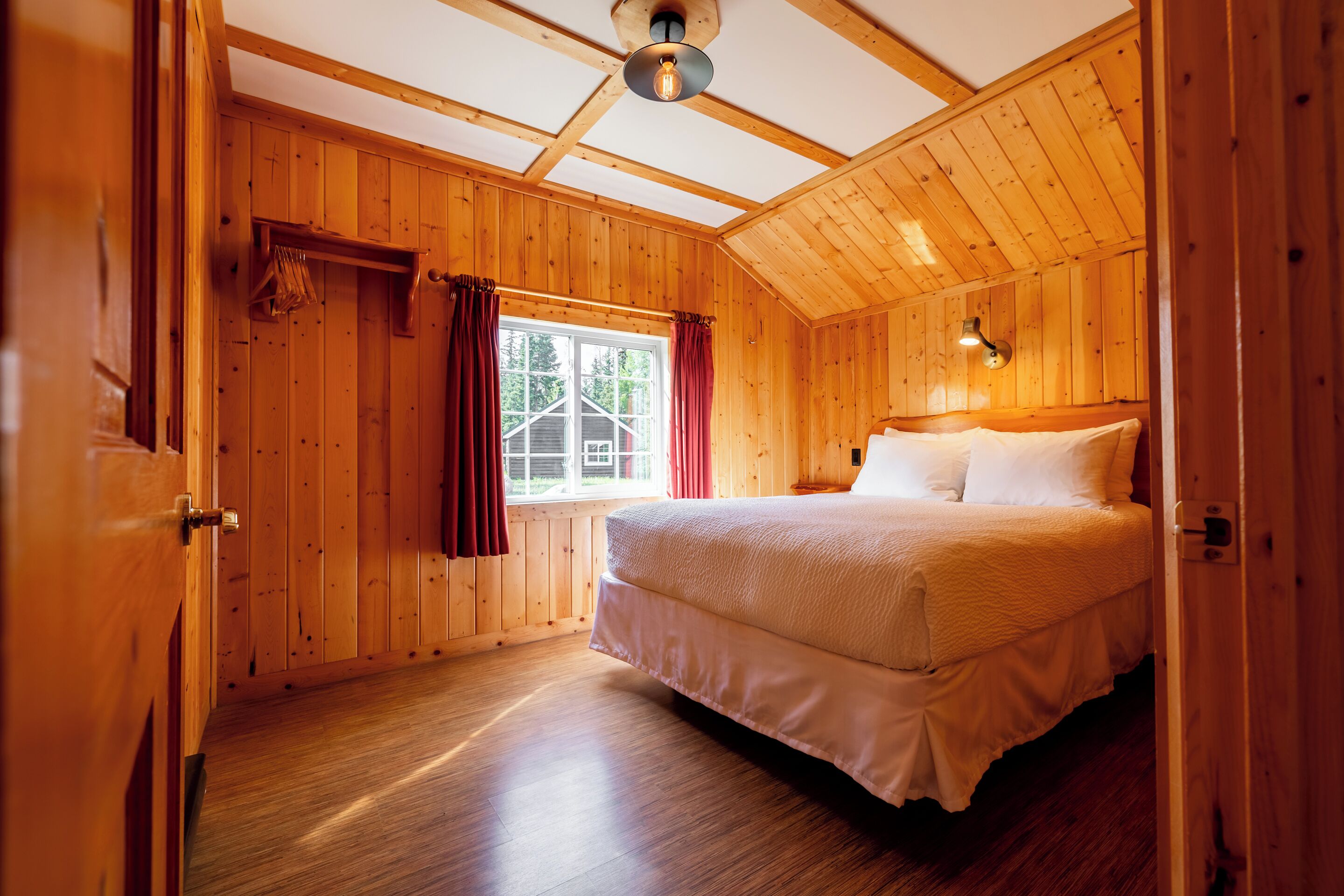 A wooden-paneled bedroom with a bed, a window with curtains, and a ceiling light fixture.