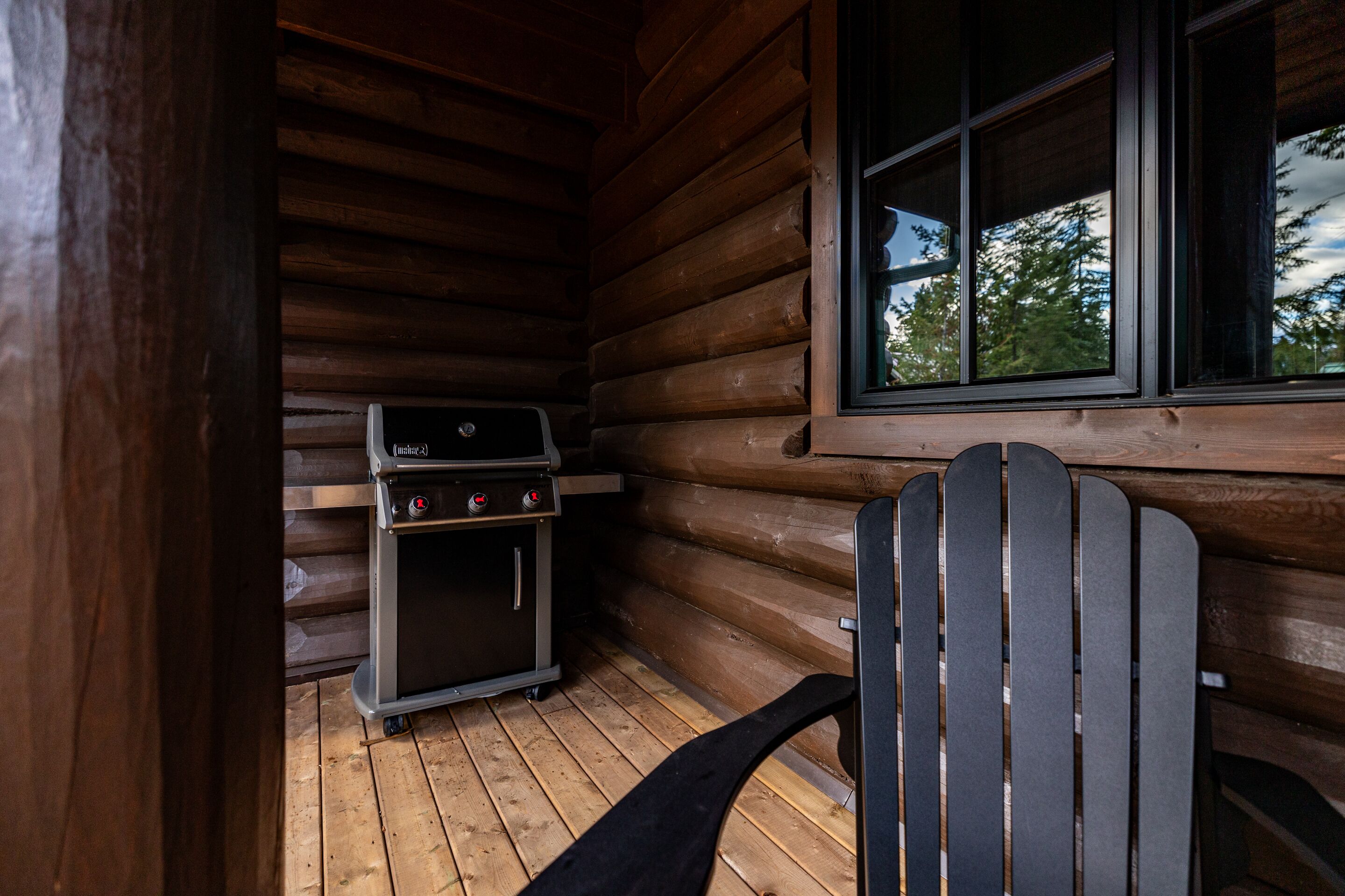 Una cabaña de madera con una parrilla y una silla cerca de una ventana.