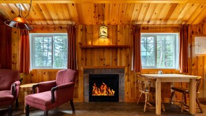 Interior acogedor de una cabaña con chimenea, paredes de madera y zona de comedor.
