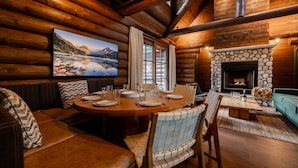 Interior acogedor de una cabaña de madera con comedor, chimenea y una ventana grande con cortinas.
