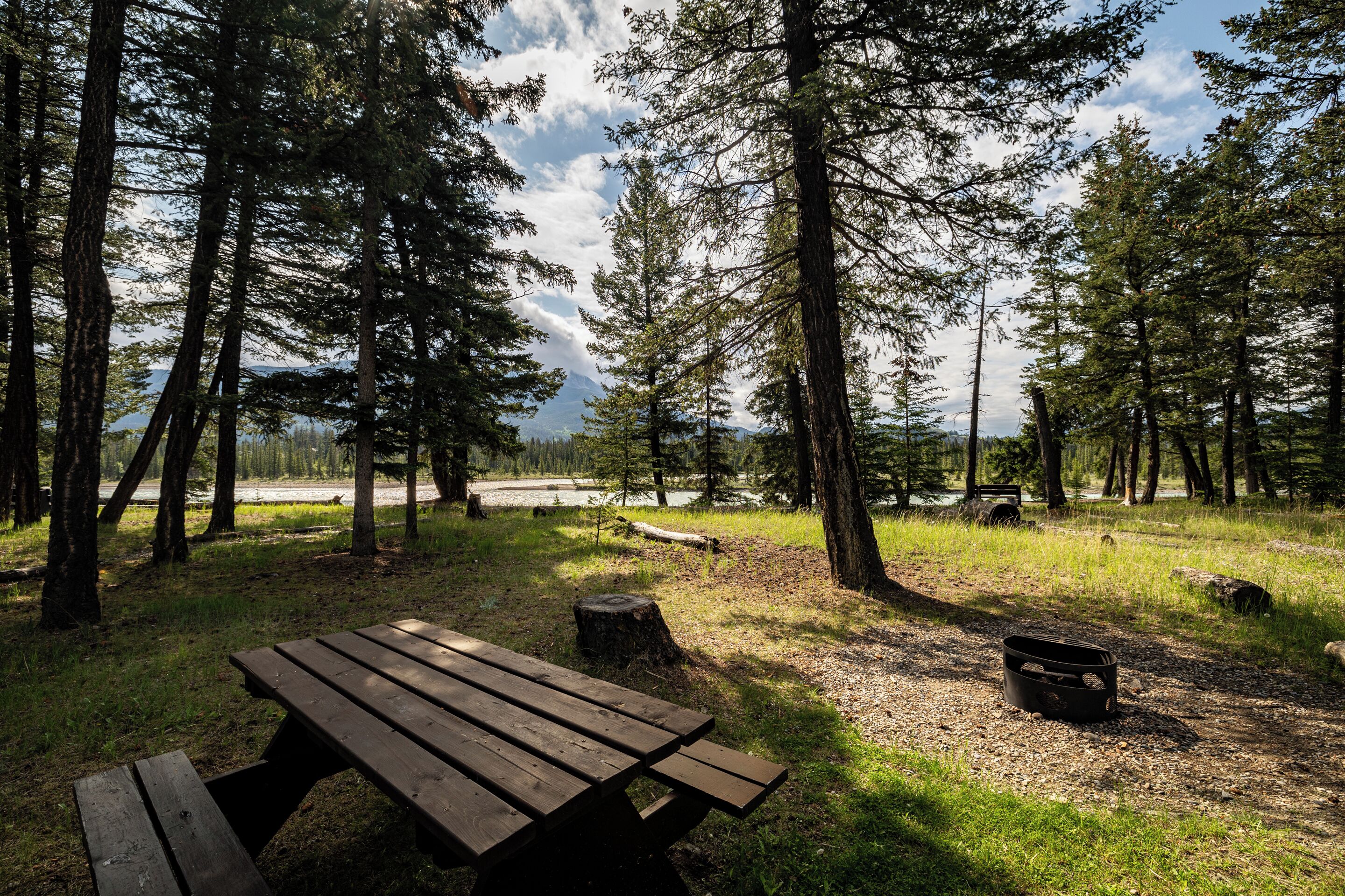 A picnic table in a forested area with a view of a lake and mountains in the background.
