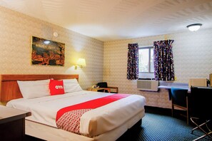 A hotel room with a bed, a desk, a chair, a lamp, a painting, and a window with curtains. - Chapmanville Inn (Chapmanville)