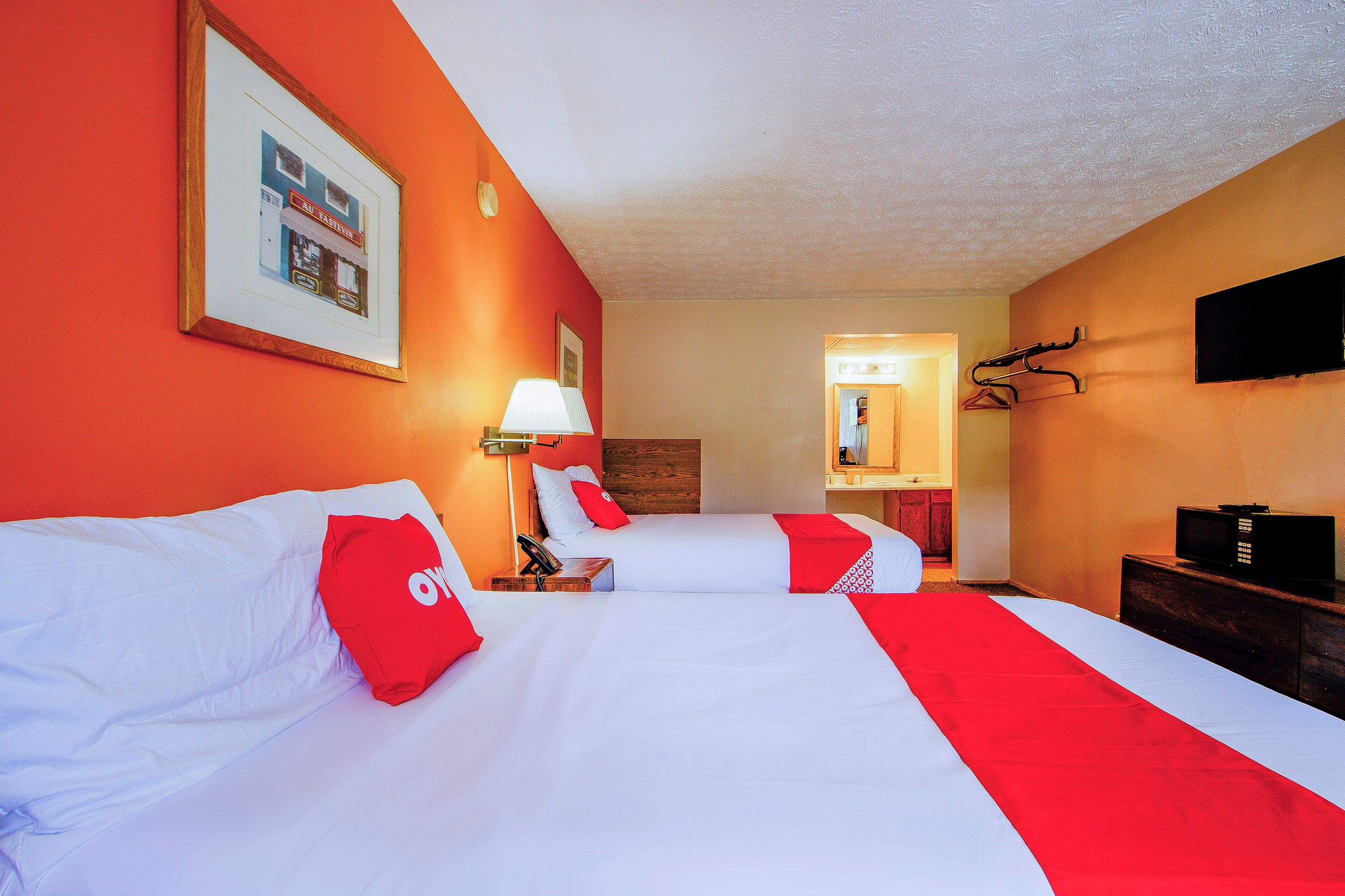 A hotel room with two beds, a television, a lamp, and a framed picture on the wall.