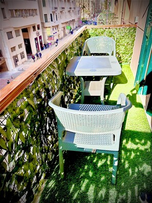A balcony with a white plastic chair and table, surrounded by green artificial grass and a metal fence. - Heritage Hostel (Cairo)