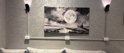Obra de arte na parede retrata um navio navegando sob uma lua cheia, com duas luminárias laterais.