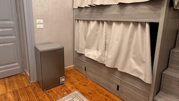 A room with a bunk bed, a small gray cabinet, a patterned rug, and a wooden floor.