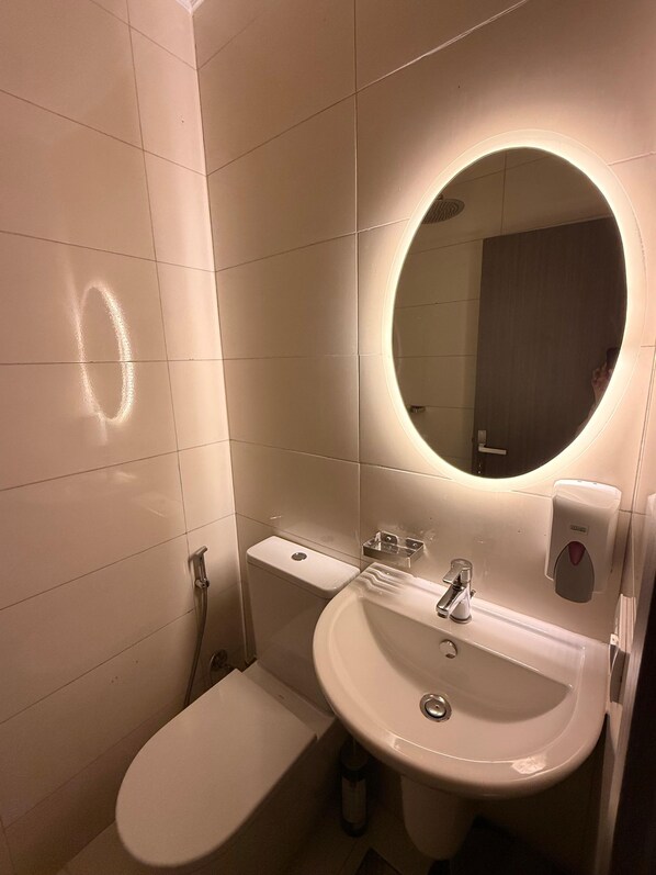 A bathroom with a toilet, sink, mirror, and hand dryer.