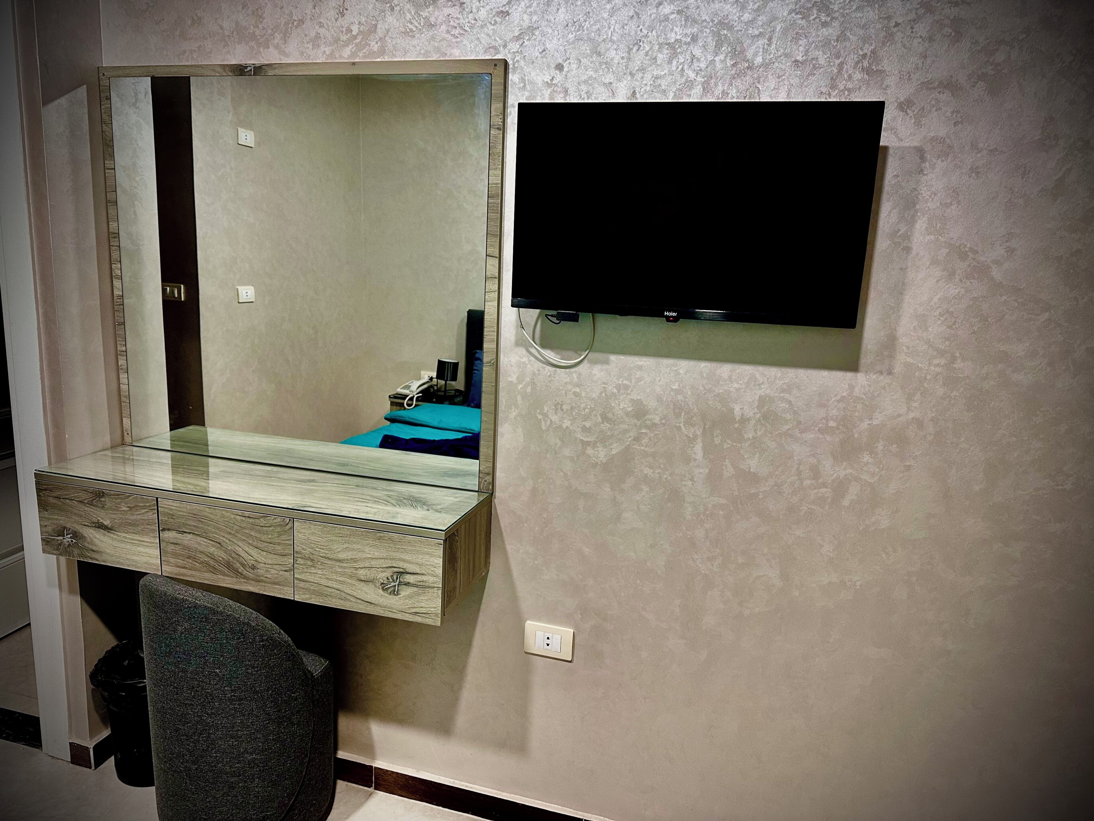Een badkamer met een glazen wastafel, een spiegel, een televisie aan de muur en een stoel.