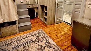 Ein Zimmer mit Holzboden, einem gemusterten Teppich, einem Bett mit Vorhang, einem Kleiderschrank, einem Spiegel und einer Tür.
