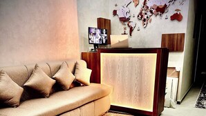 Ein modernes Wohnzimmer mit einer Couch, einem gemusterten Teppich, einem Holztresen zur Rezeption, einer Weltkarte an der Wand und einer Klimaanlage.
