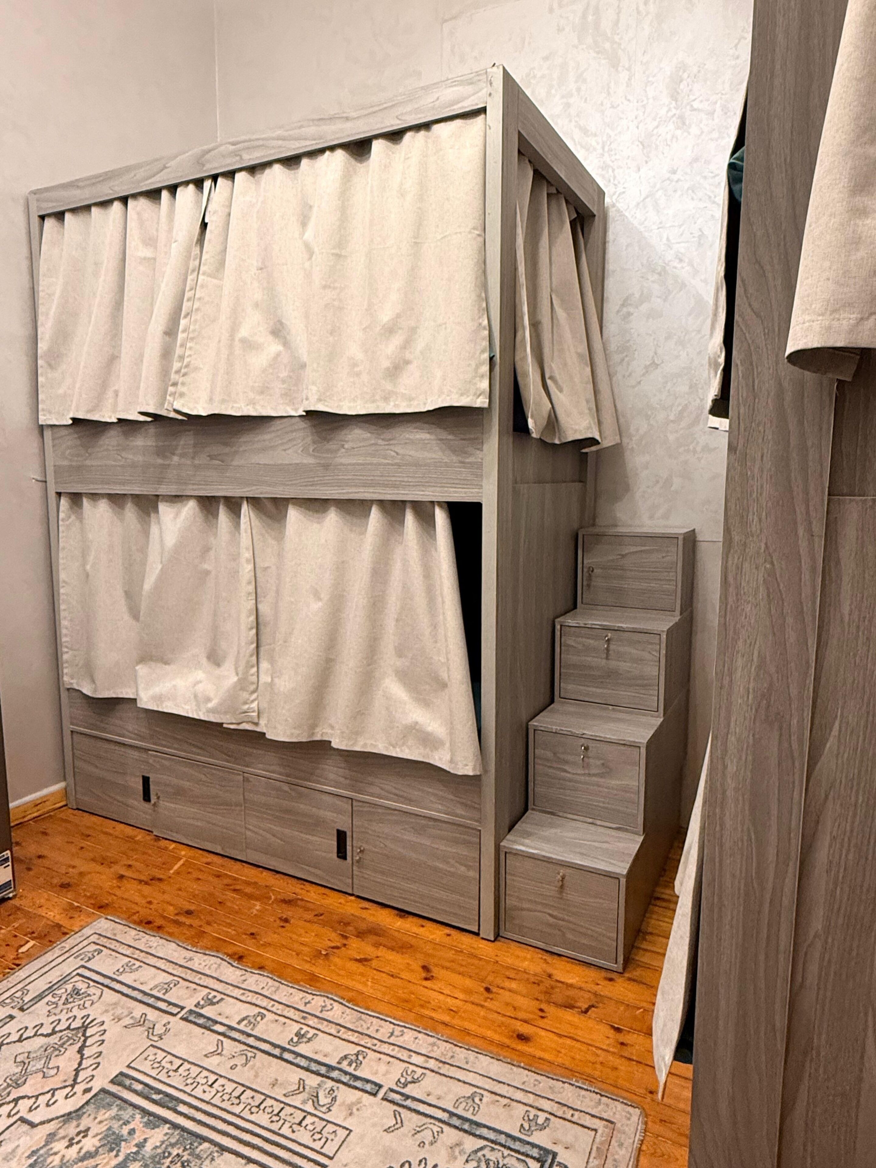 Ein Stockbett mit Holzrahmen, zwei Vorhängen und einer kleinen Kommode.