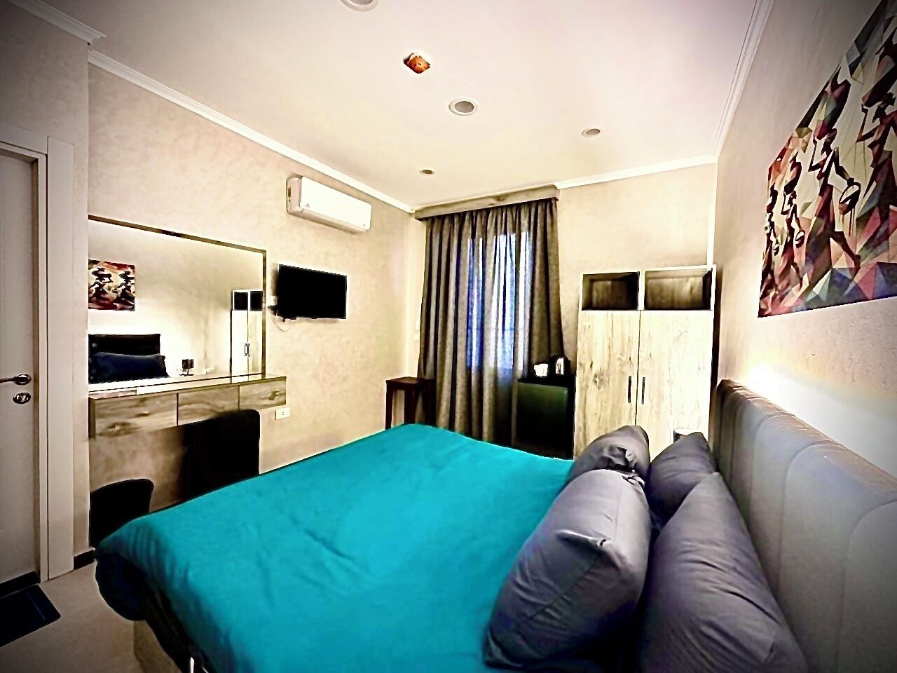 A hotel room with a bed, a sofa, a desk, a mirror, and a window with curtains.