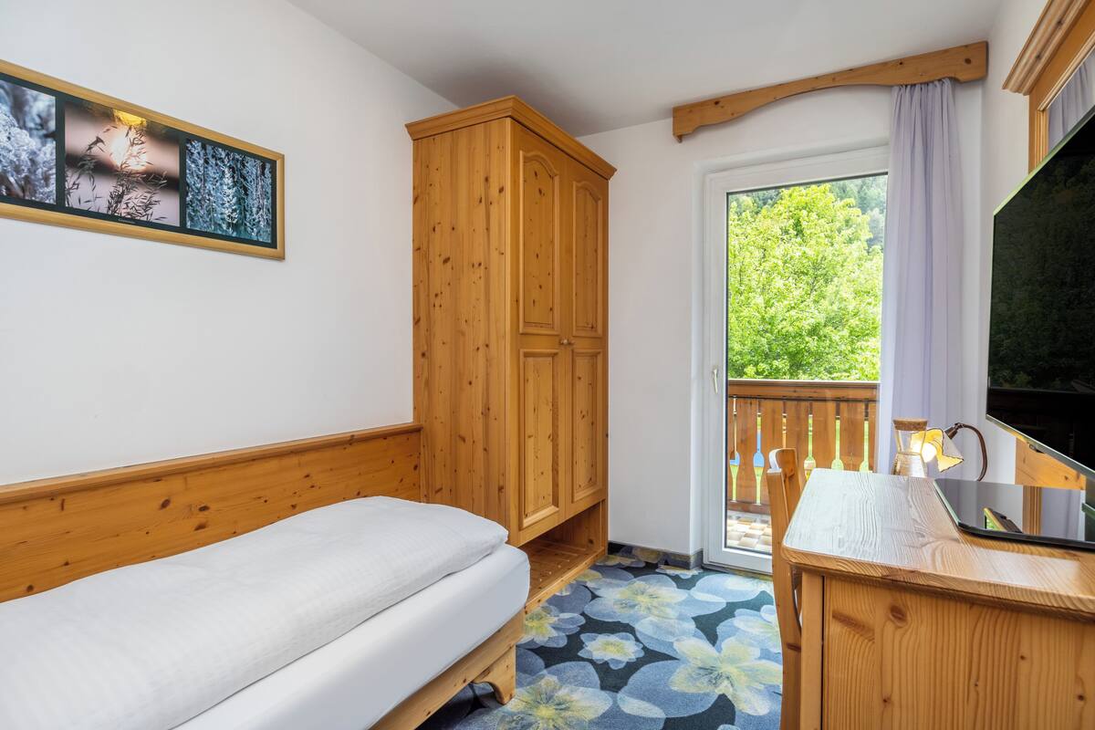 A bedroom with a bed, wooden wardrobe, and a balcony with a view of greenery.