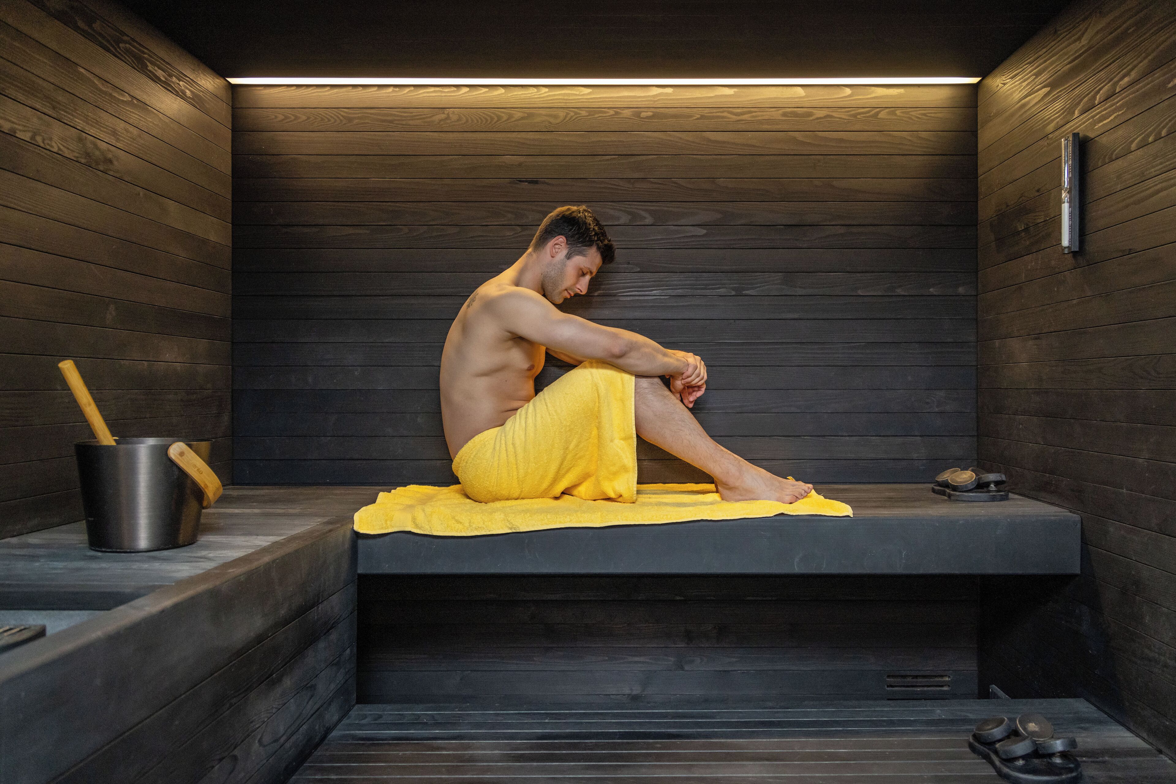 Un sauna avec un intérieur en bois, un banc et une personne assise dessus.