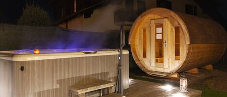 A hot tub and a wooden barrel sauna with a wooden deck and steps leading to the hot tub.