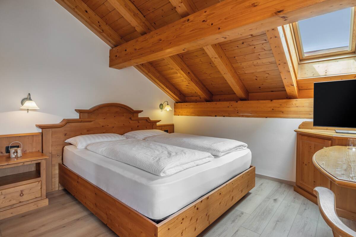A wooden bedroom with a bed, bedside table, lamp, and a TV.