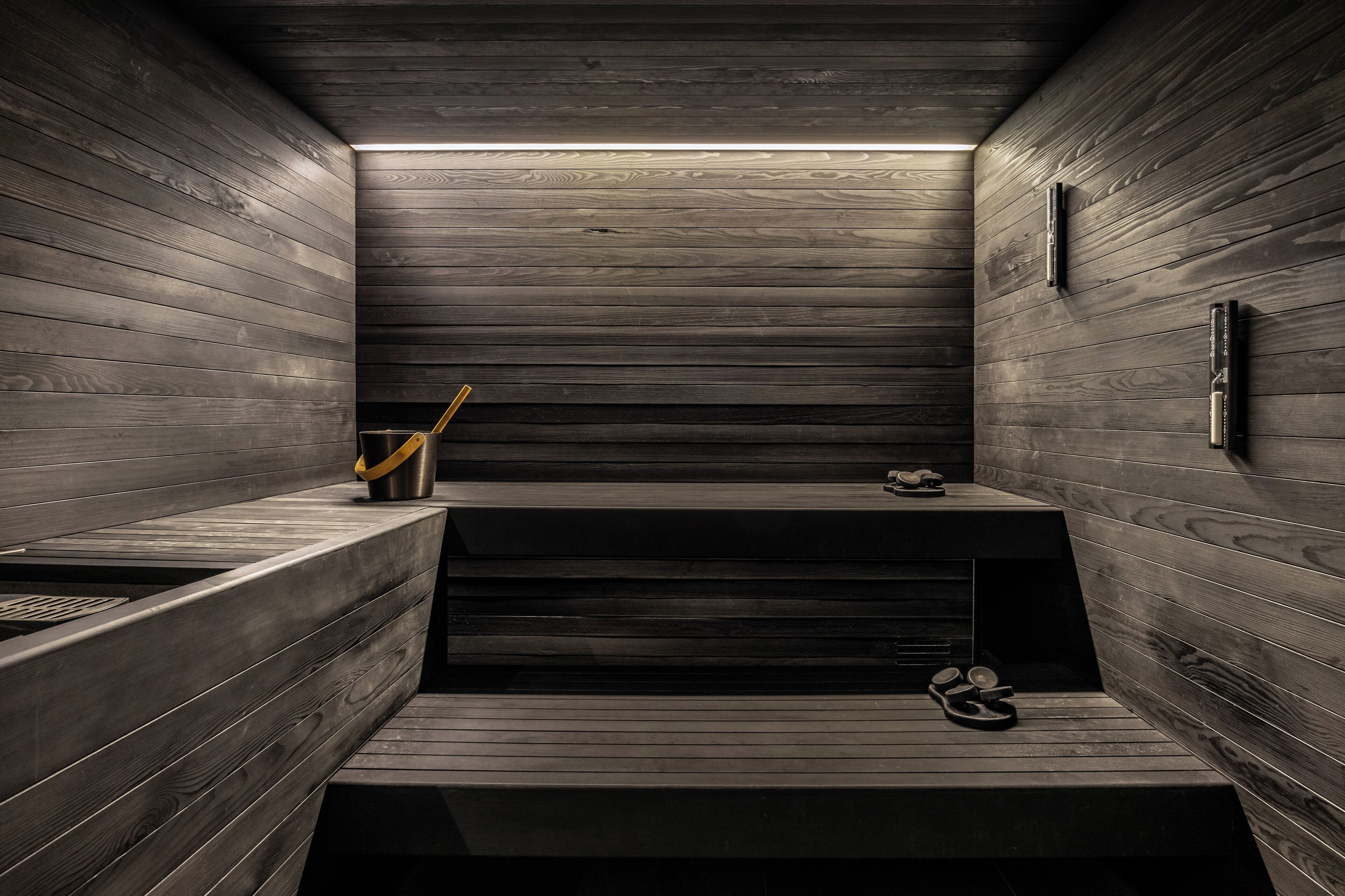 A wooden interior with a bench, a trash bin, and a pair of slippers.