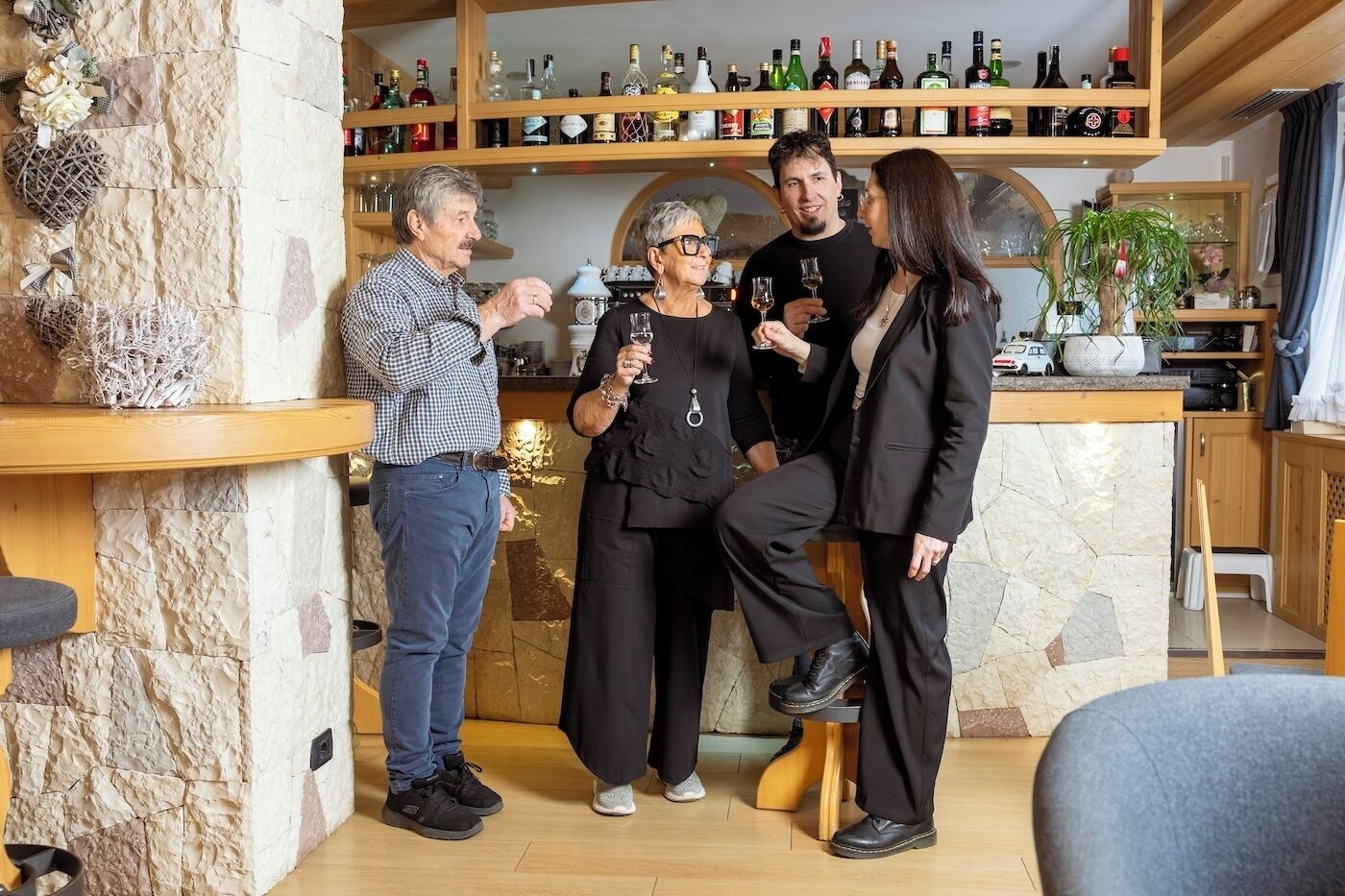 Un grupo de personas en una habitación con pared de piedra, estantes de madera con botellas y una pequeña mesa.
