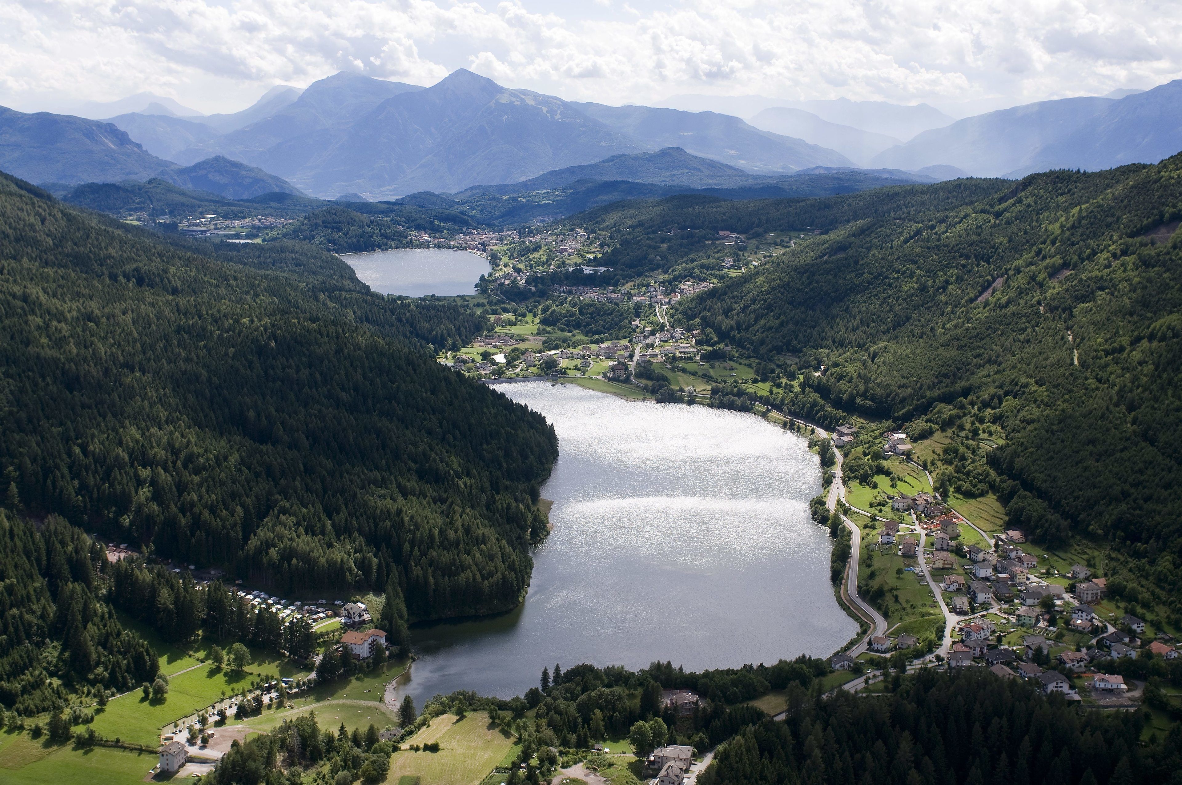 A lakeside village with a central road, surrounded by forested hills and mountains.