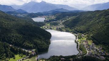 A lakeside village with a central road, surrounded by forested hills and mountains.