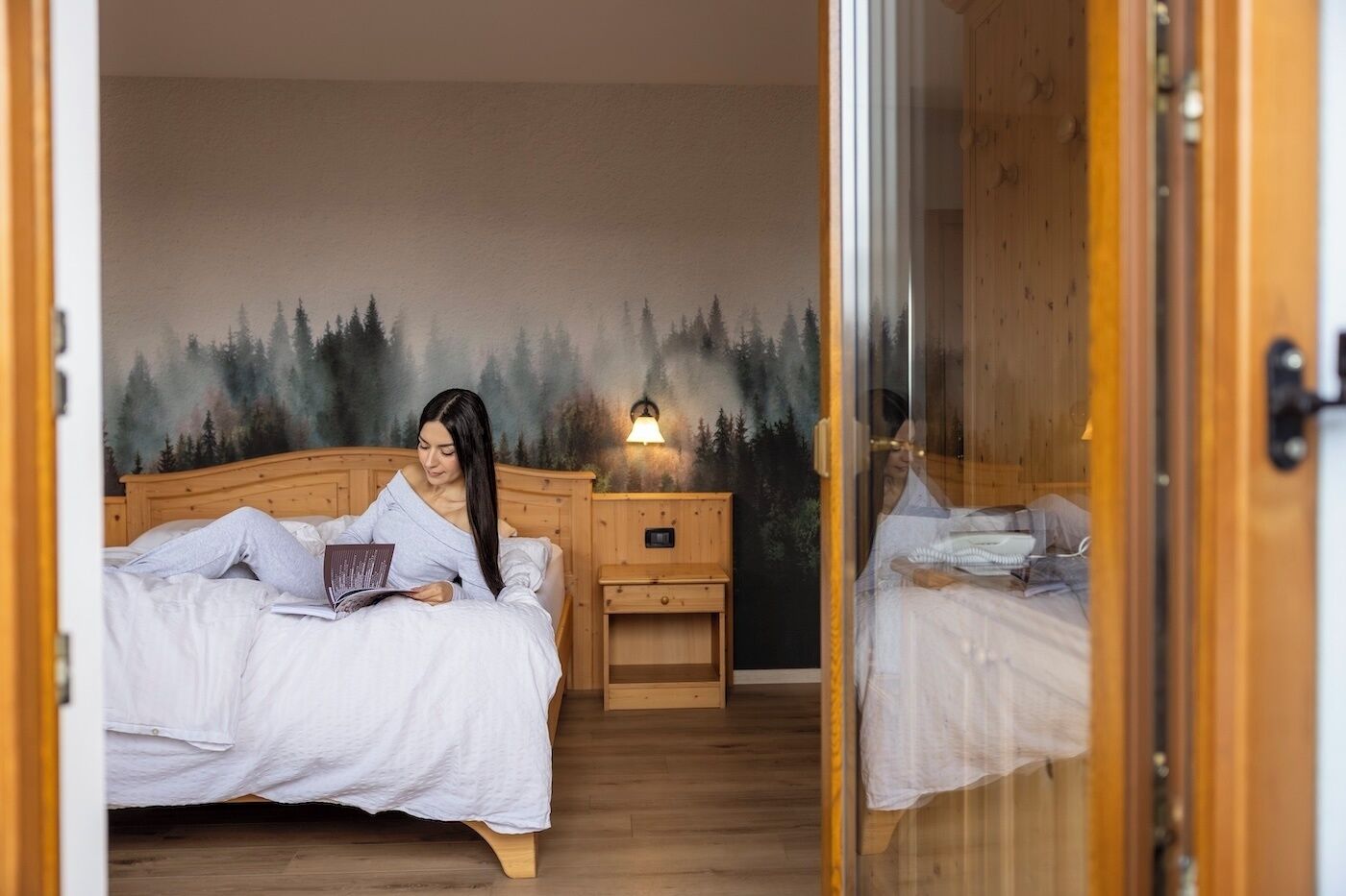 A bedroom with a bed, a nightstand, a wall-mounted lamp, and a mirror.