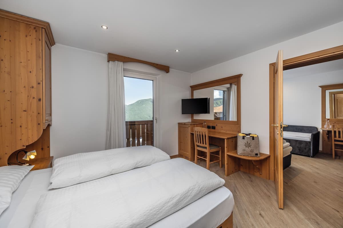 A bedroom with a bed, a desk with a chair, a television, and a view of the outdoors.