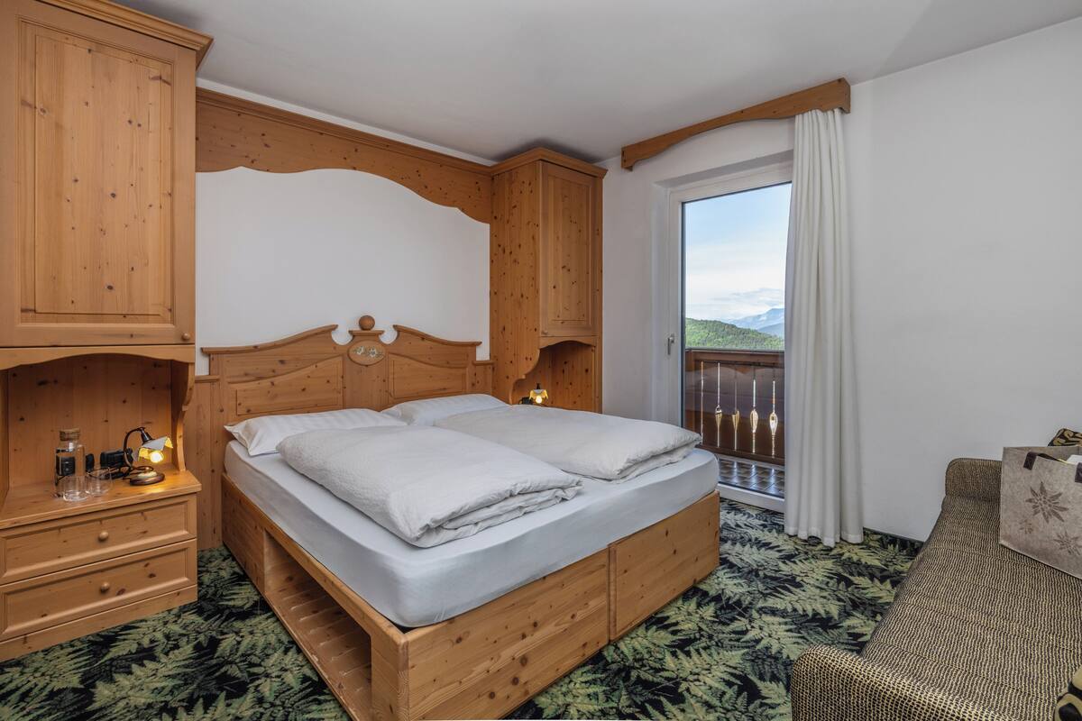 A wooden bed with a headboard, a nightstand with a lamp, and a view of a balcony.