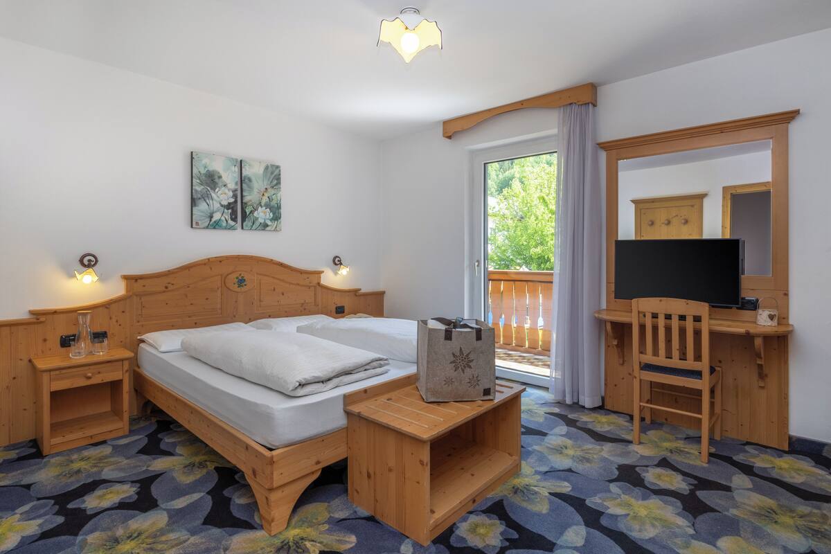 A hotel room with a wooden bed, a desk with a chair, a television, and a window with curtains.