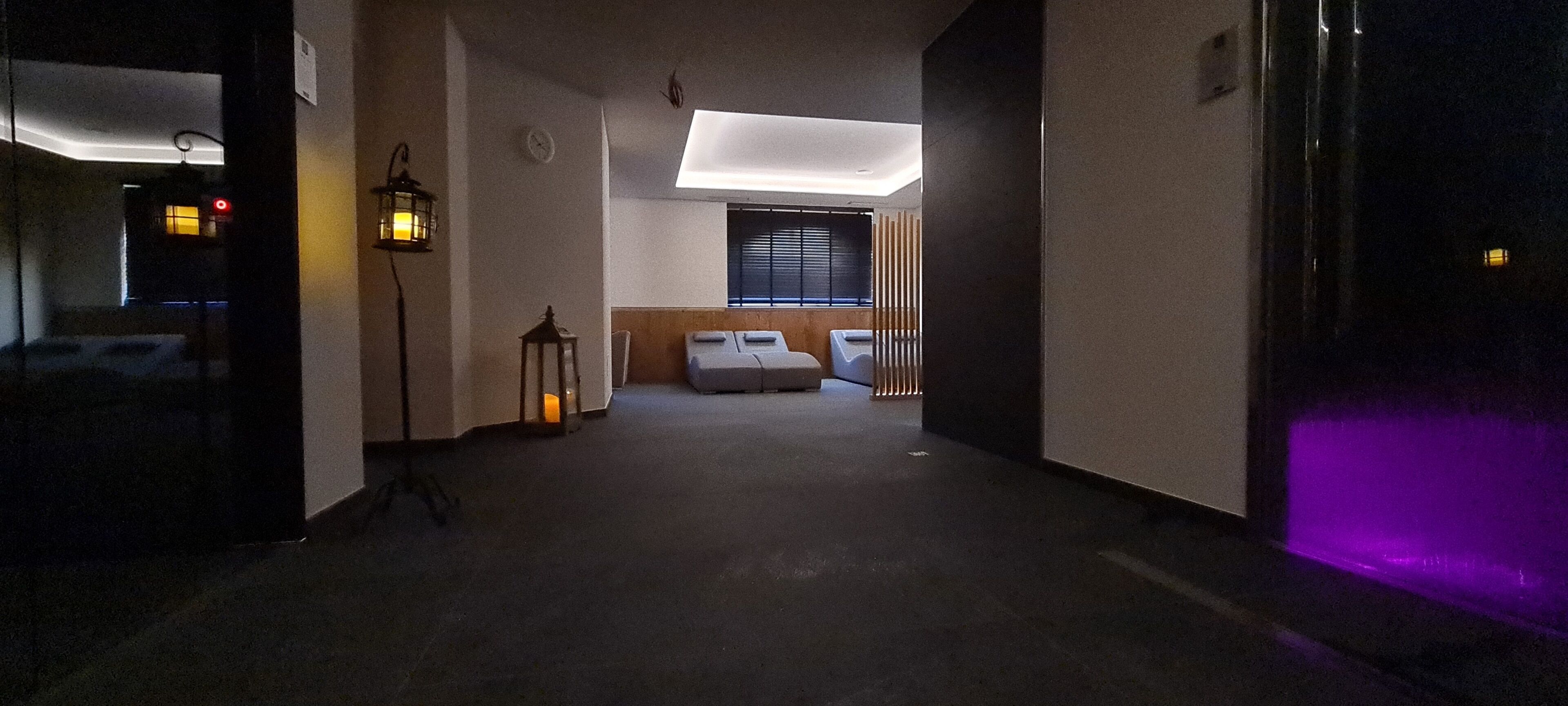 A hallway with a bed, a small table, and a wall-mounted clock.