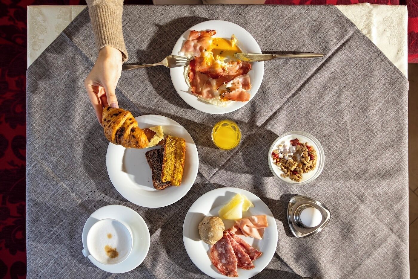 A breakfast spread on a table with plates of food, a croissant, and a glass of juice.