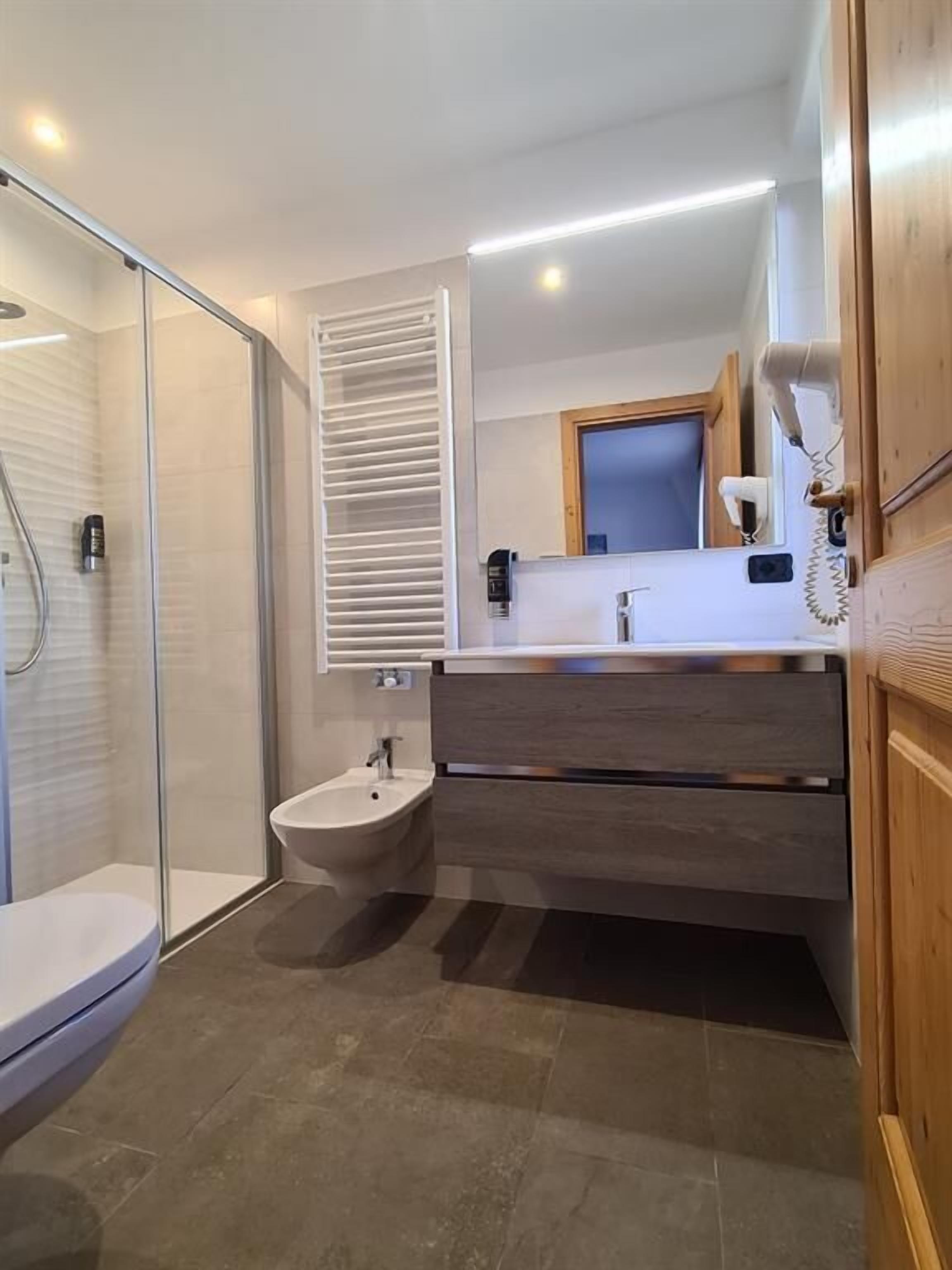 Une salle de bain moderne avec une douche à parois de verre, un lavabo sur colonne et un meuble-lavabo avec un miroir.