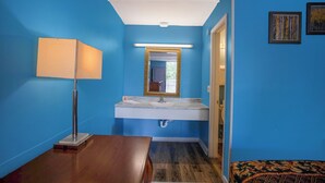 Une salle de bain aux murs bleus, avec un lavabo blanc, un miroir à cadre doré, une table en bois et un lit à motifs.