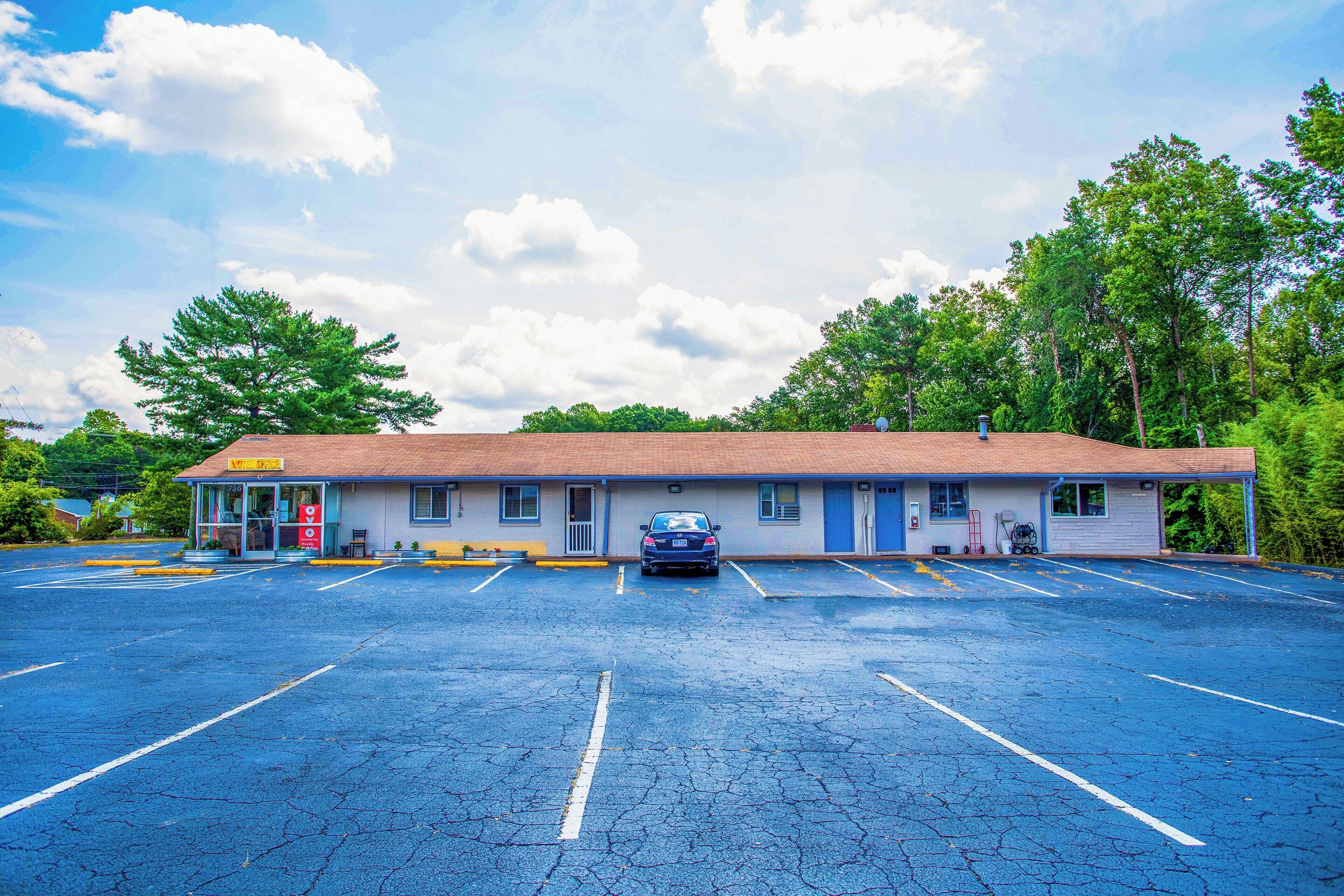 A motel with a parking lot, a car parked in front, and a building with a red roof.