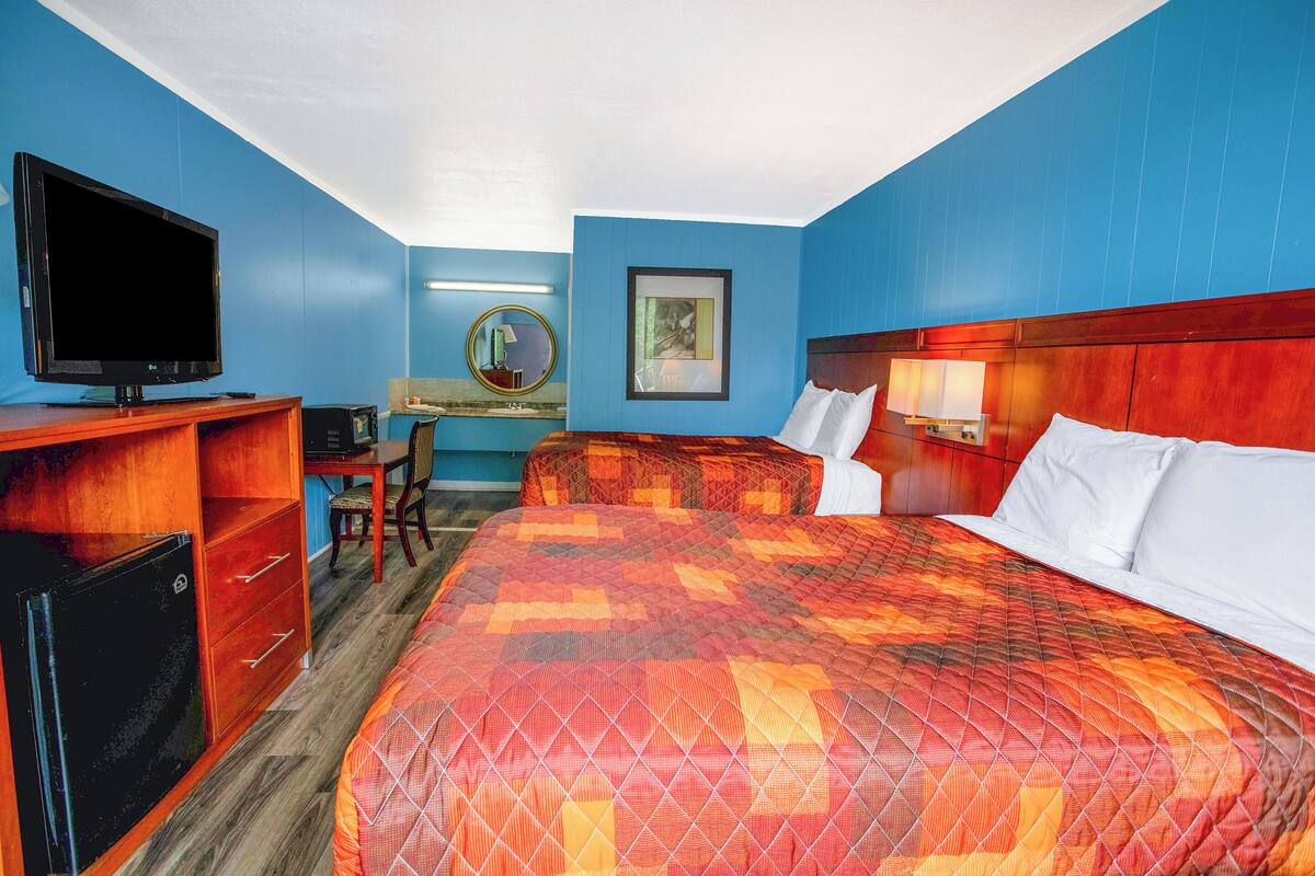 Ein Hotelzimmer mit einem großen Bett, einem Schreibtisch mit Computer, einem Fernseher und einem kleinen Kühlschrank.