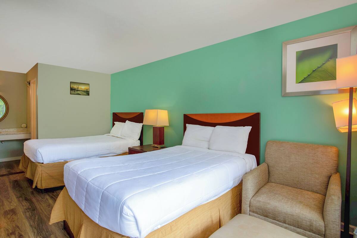Ein Hotelzimmer mit zwei Betten, Holzboden, grüner Wand und einem gerahmten Bild.