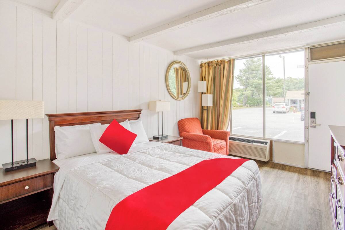 Ein Hotelzimmer mit einem großen Bett, einem Sessel, einem Spiegel und Blick ins Freie.
