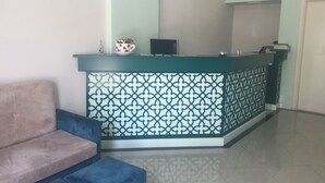 A reception area with a patterned counter, a blue sofa, and a tiled floor. - Lukas Hotel (Xhafzotaj)
