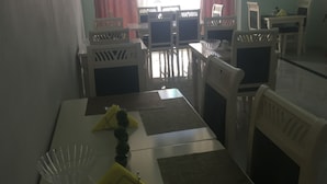 A dining area with a table set for four, surrounded by white chairs with patterned backs. - Lukas Hotel (Xhafzotaj)