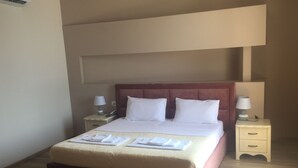 A hotel room with a large bed, two bedside tables with lamps, a wooden floor, and a small table with towels. - Lukas Hotel (Xhafzotaj)
