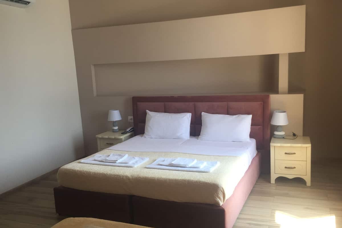 A hotel room with a large bed, two bedside tables with lamps, a wooden floor, and a small table with towels.