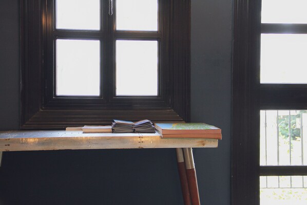 A window with a view of greenery outside, a table with books, and a painting easel.