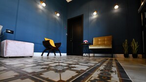 Una habitación con pared azul, piso estampado, un sofá, una silla y una mesita con una flor.