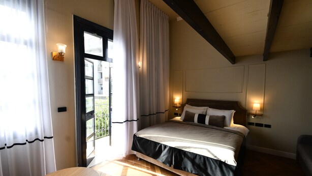 Un dormitorio con cama, lámparas de noche, una ventana con cortinas y una mesa de madera.